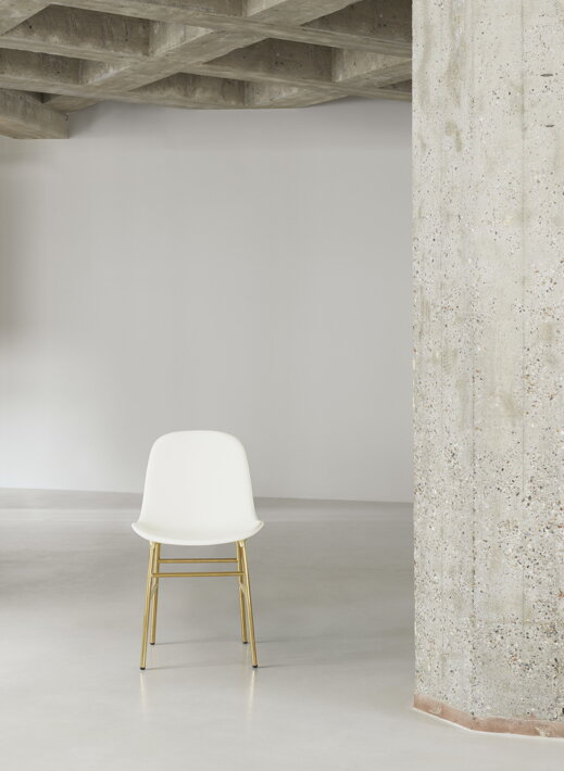 Biela jedálenská stolička s mosadznými nohami pri múriku v hale