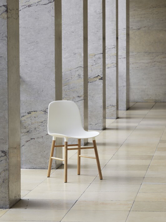 Biela jedálenská stolička s dubovými nohami pri múriku v hale