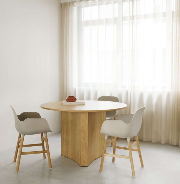 Tri sivé jedálenské stoličky za okrúhlym dreveným jedálenským stolom vo svetlej jedálni vedľa veľkého okna