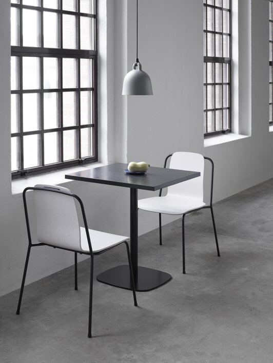Malý kaviarenský stôl so štvorcovou stolovou doskou z čierneho dubu s dvoma stoličkami na svetlej chodbe pred veľkými oknami