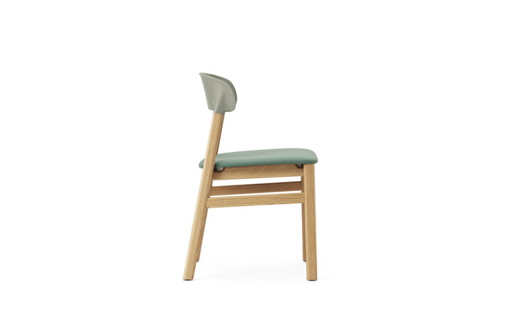 Detail bočnej strany zelenej jedálenskej stoličky s dubovými nohami a s čalúnením