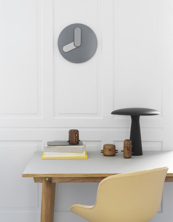 Masívna drevená figúrka papagáj na pracovnom stole pod dizajnovými nástennými hodinami