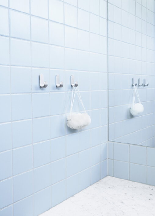 Tri matné strieborné háčiky s uterákom v modrej kúpeľni pri zrkadle