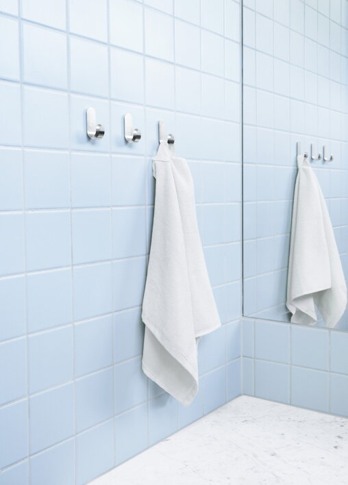 Tri lesklé strieborné háčiky s uterákom v modrej kúpeľni pri zrkadle