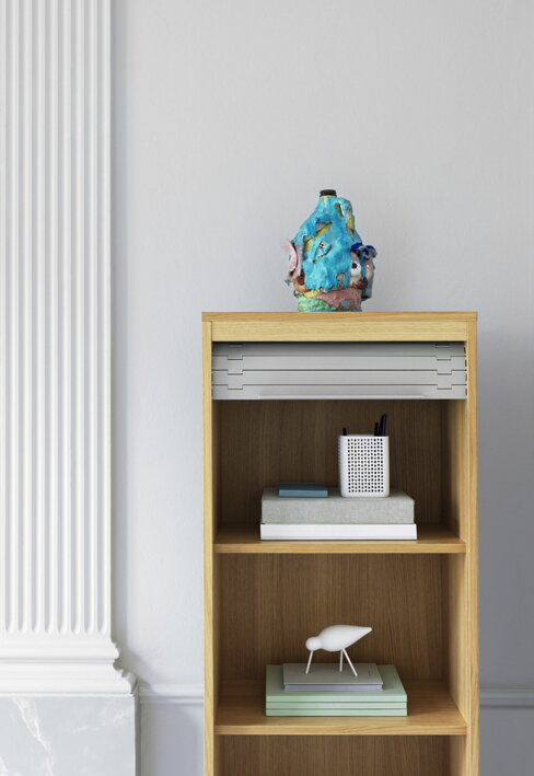 Stredný dekoračný vtáčik z dubu v bielej farbe s bielymi kovovými nohami na polici pod dizajnovou vázou