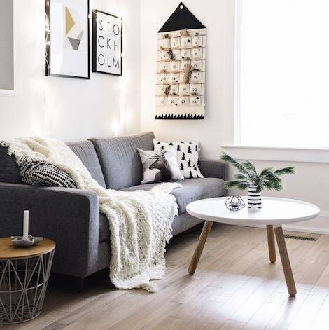 Stolík v obývačke pred sivou pohovkou cez ktorú je prehodená krémová deka