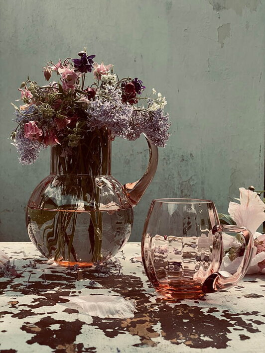 Krištáľový ružový pohár na pivo Marie pri sklenenej váze s kvetmi