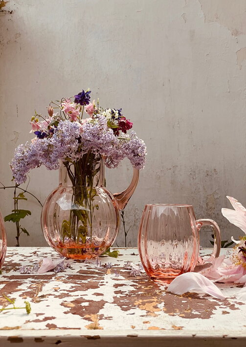 Krištáľový veľký pohár na pivo Marie v ružovej farbe pri váze s naaranžovanými kvetmi