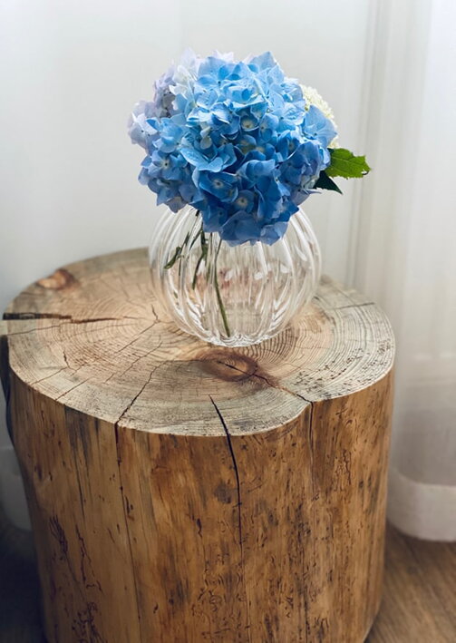 Modrá hortenzia v malej čírej váze z ručne fúkaného krištáľu na drevenom pníku