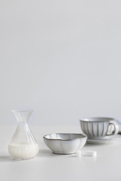 Veľká mini karafa s mliekom na stole pri keramickej miske a šálke s kávou