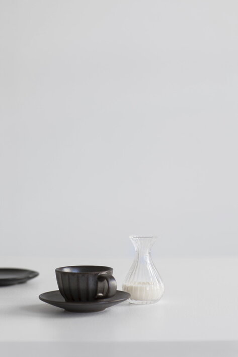 Malá mini karafa s mliekom na stole pri čiernej šálke s kávou