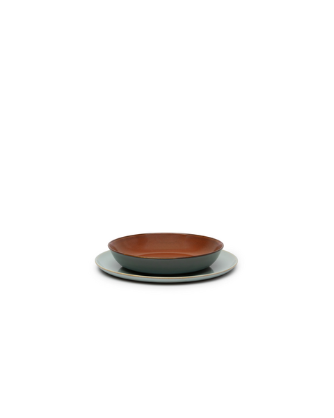 Malý sivomodrý hlboký tanier s červenohnedým vnútrom položený na plytkom sivomodrom tanieri.