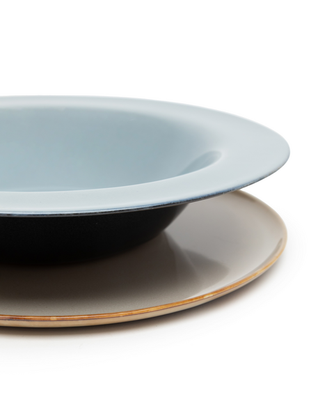 Veľký tmavomodrý tanier na cestoviny so sivomodrým vnútrom položený na plytkom tanieri v pieskovej farbe