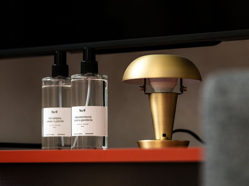Dva bytové parfumy pri mosadznej stolovej lampe.