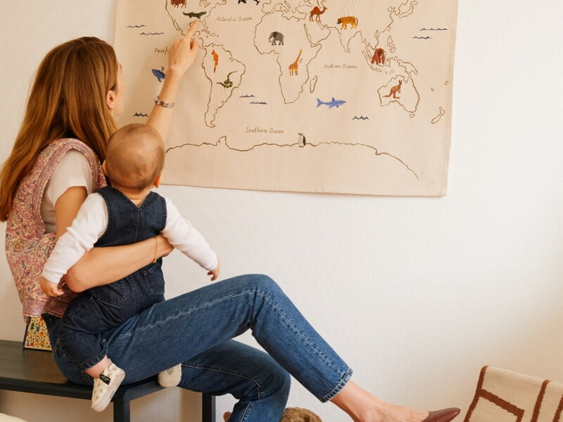 Mama s bábätkom v náručí pozerajúce sa na látkovú mapu sveta so zvieratkami.