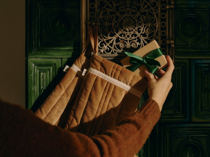 Ruka vkladajúca darček so zelenou stuhou do jednej z vianočných ponožiek.