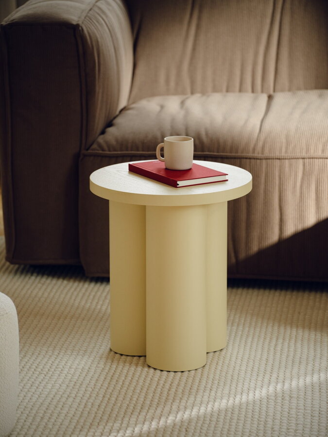 Svetložltý príručný stolík, na ktorom je položená kniha a biela šálka.