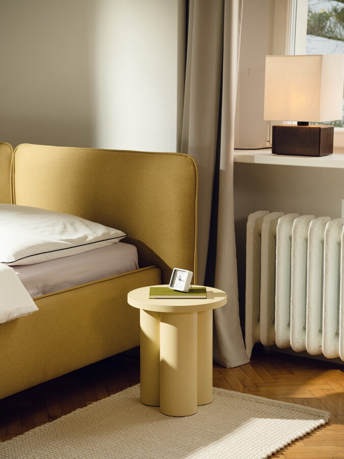 Svetložltý príručný stolík, na ktorom je položená kniha a budík.