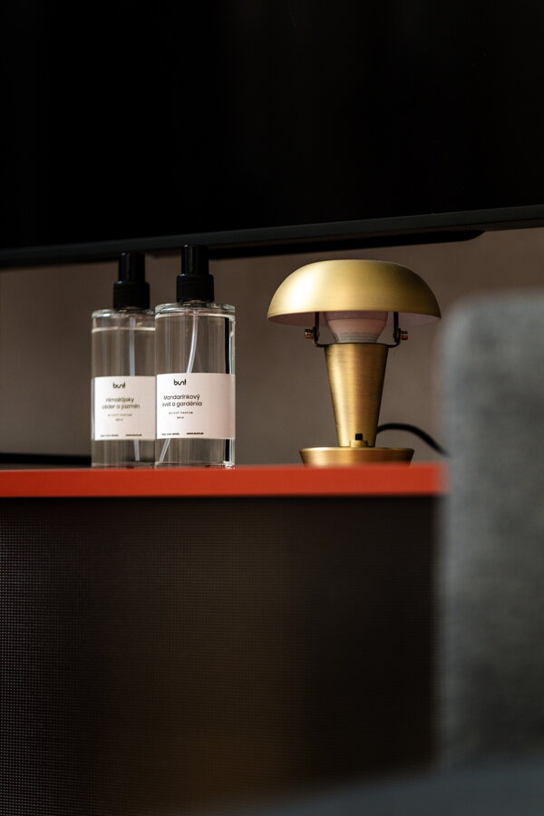 Dve sklenené fľaštičky bytového parfumu na stolíku vedľa mosadznej stolovej lampy.