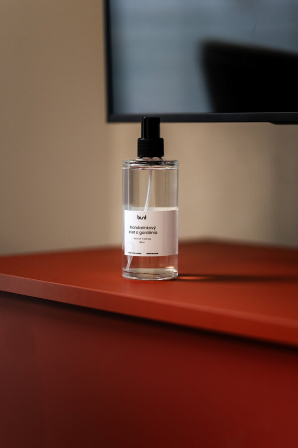 Bytový parfum s vôňou mandarínkového kvetu a gardénie v čírej sklenenej fľaštičke na červenej komode.