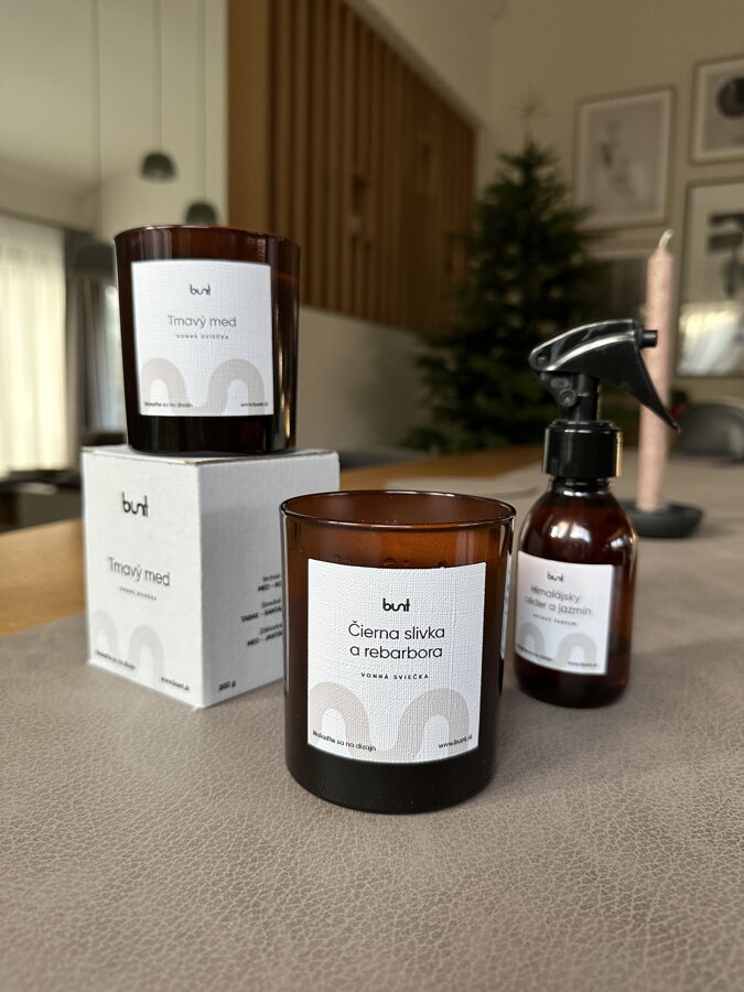 Vonná sviečka v tmavohnedom pohári a bytový parfum v spreji na jedálenskom stole v pozadí so sviečkou