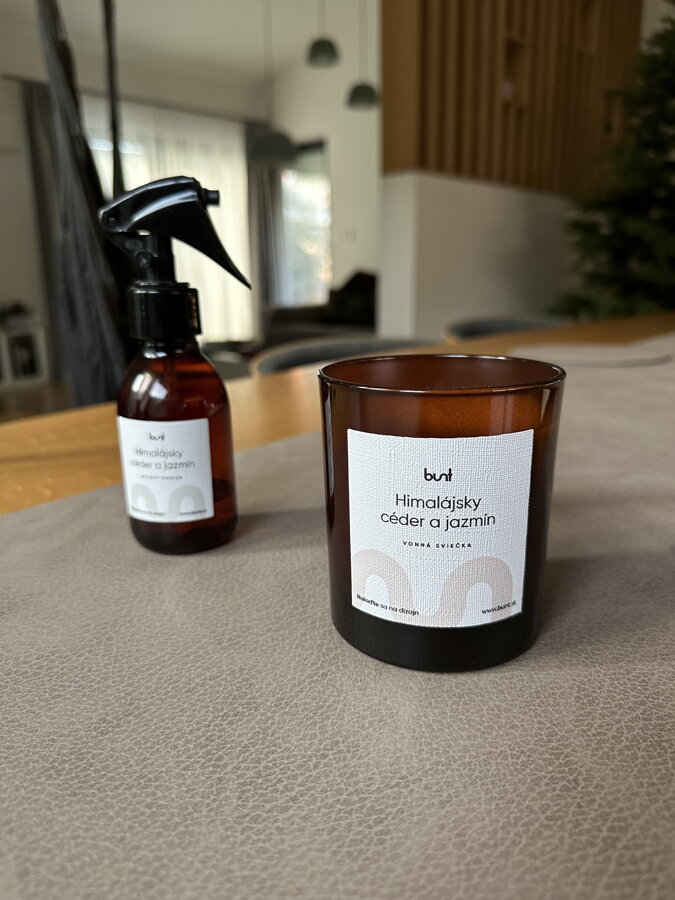 Bytový parfum v spreji a vonná sviečka v hnedom sklenonom pohári s vôňou himalájskeho cédra a jazmínu na jedálenskom stole