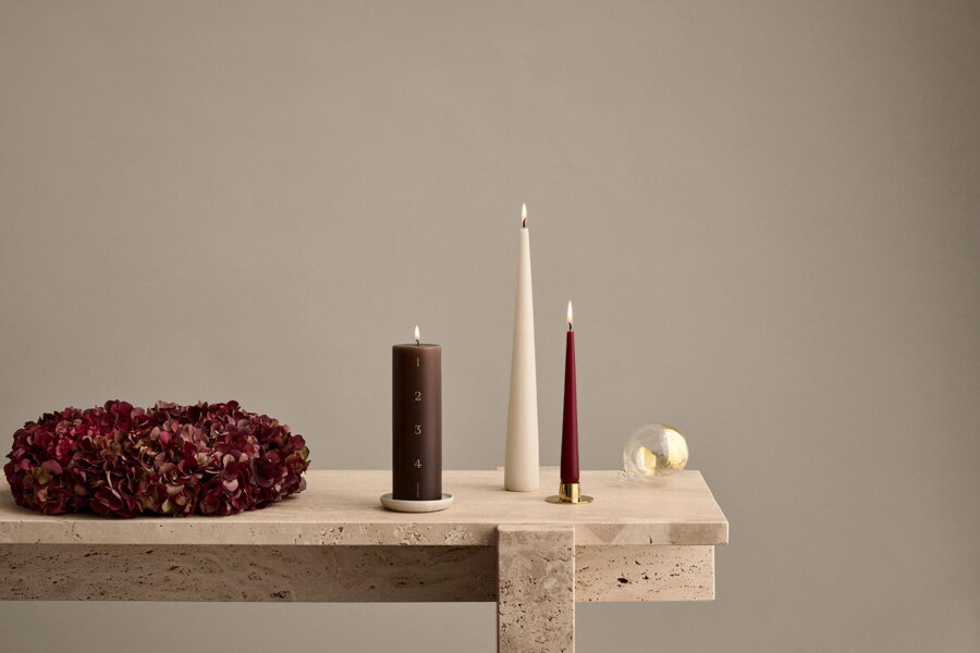 Hnedá adventná sviečka na svetlom stole vedľa tmavočerveného adventného venca a dalších dvoch sviečok.