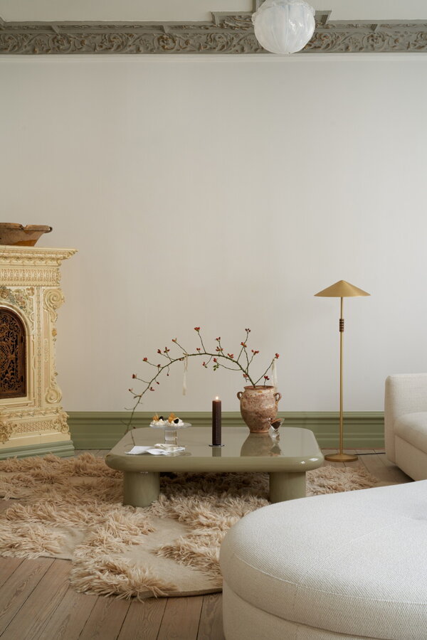 Horiaca hnedá adventná sviečka na konferenčnom stolíku vedľa vázy s vetvičkou v obývačke s krbom.