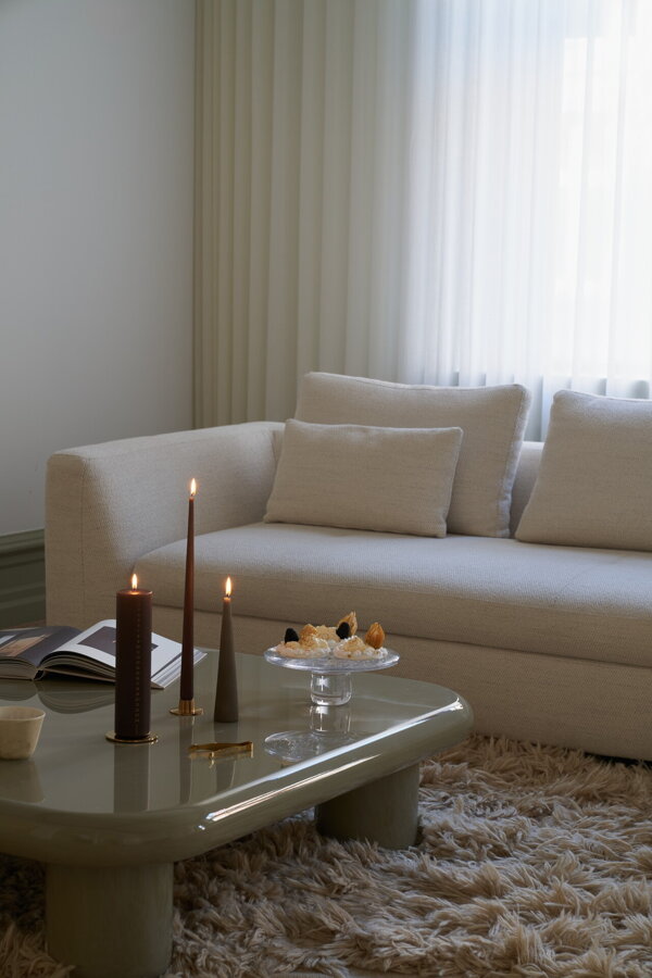 Tri horiace sviečky v obývačke na konferenčnom stolíku pred béžovou pohovkou.