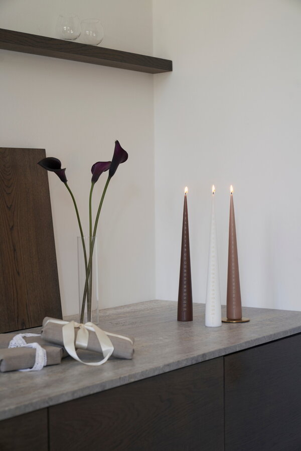 Dve horiace kónické sviečky na stolíku s vázou a kvetmi.