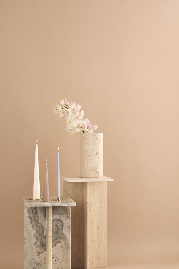 Dve horiace kónické sviečky svetlohnedej a bielej farby na mramorovom podstavci.