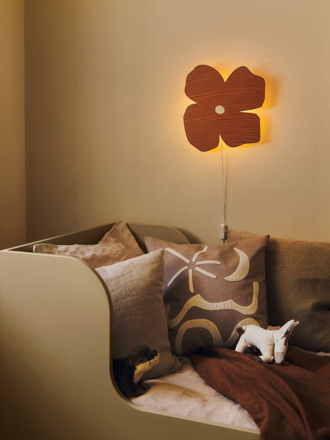 Hnedá nástenná lampa v tvare kvetu upevnená na stenu nad detskou posteľou.