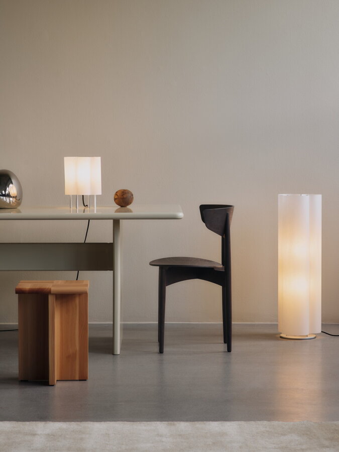 Vysoká biela stojanová lampa vedľa bieleho písacieho stola s tmavohnedou drevenou stoličkou.
