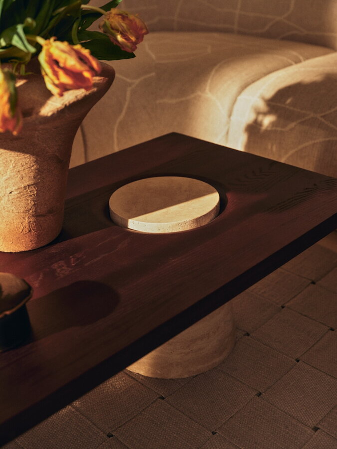 Luxusný konferenčný stolík s obdĺžnikovou stolovou doskou, vyrobený z travertínu a karbonizovaného jaseňa, na ktorom je položená váza s kvetmi.