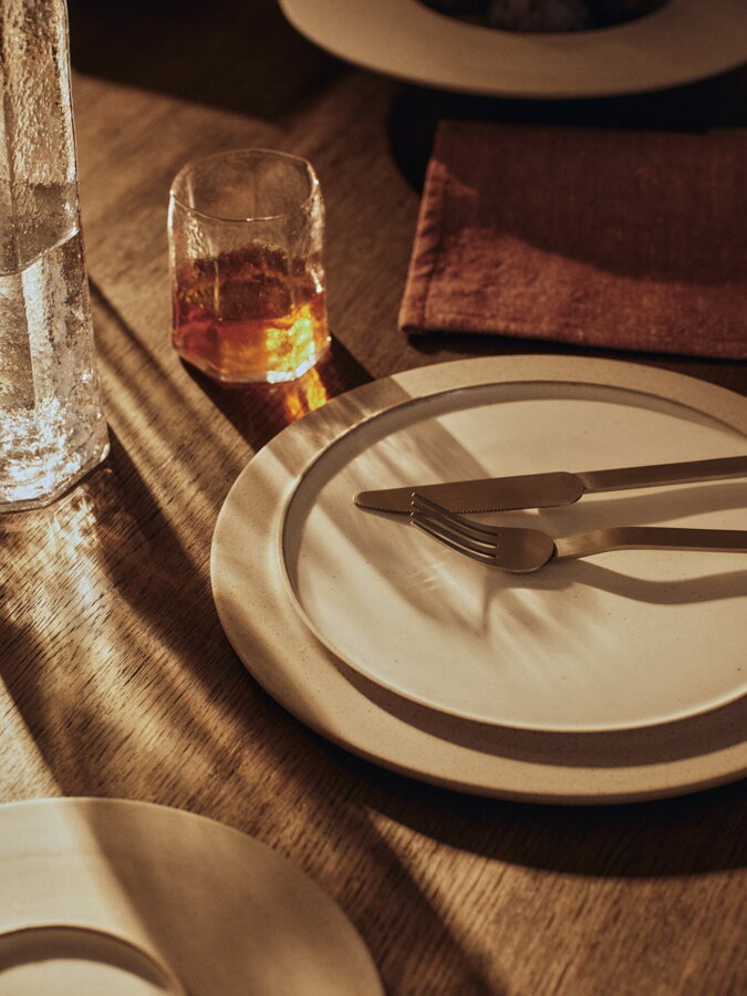 Sklenený pohár a karafa na prestretom stole vedľa kameninových tanierov.