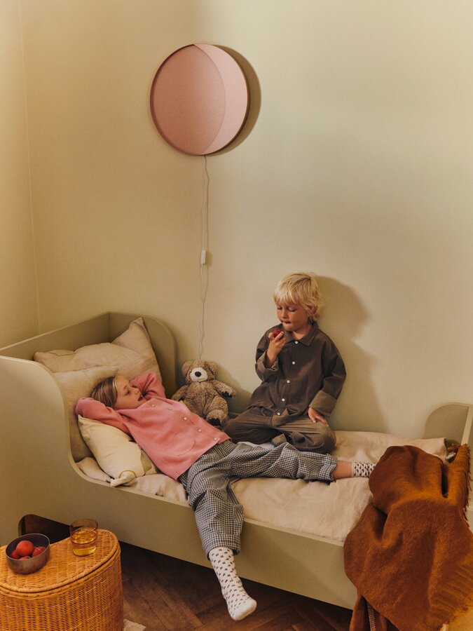 Deti hrajúce sa na posteli, nad ktorou je lampa Neba ružovej farby.