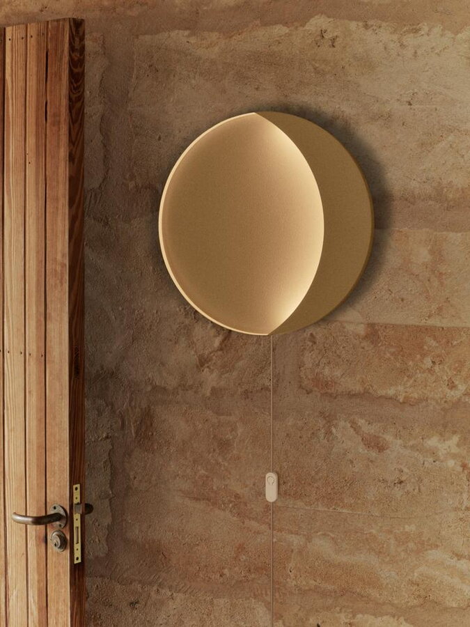 Okrúhla nástenná lampa s výrezom v tvare polmesiaca zavesená na stene vedľa dverí.