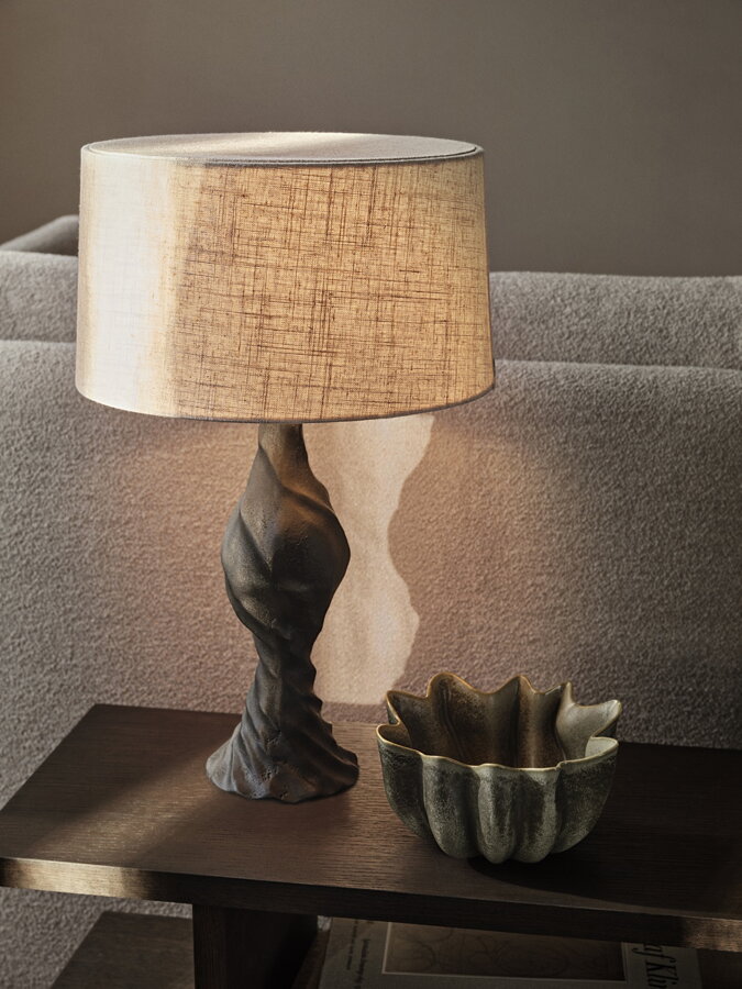 Tmavozelená kameninová misa Nium s dizajnom nariasenej textílie, na stolíku vedľa svietiacej stolovej lampy.