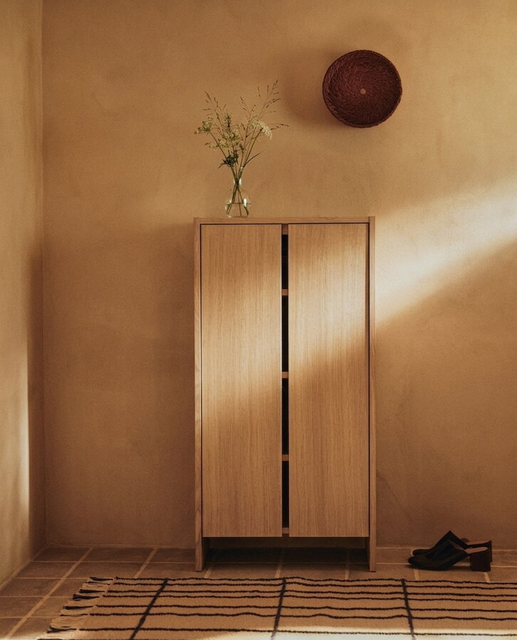 Vysoká predsieňová skrinka Parcel s výklopnými policami, z dubového dreva prírodnej farby v predsieni vedľa topánok na podlahe.