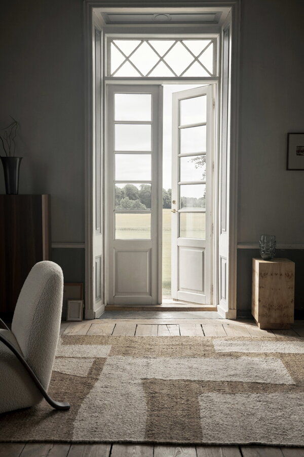 Bielo hnedý vlnenžý koberec v miestnosti s veľkými bielymi presklenými dverami.