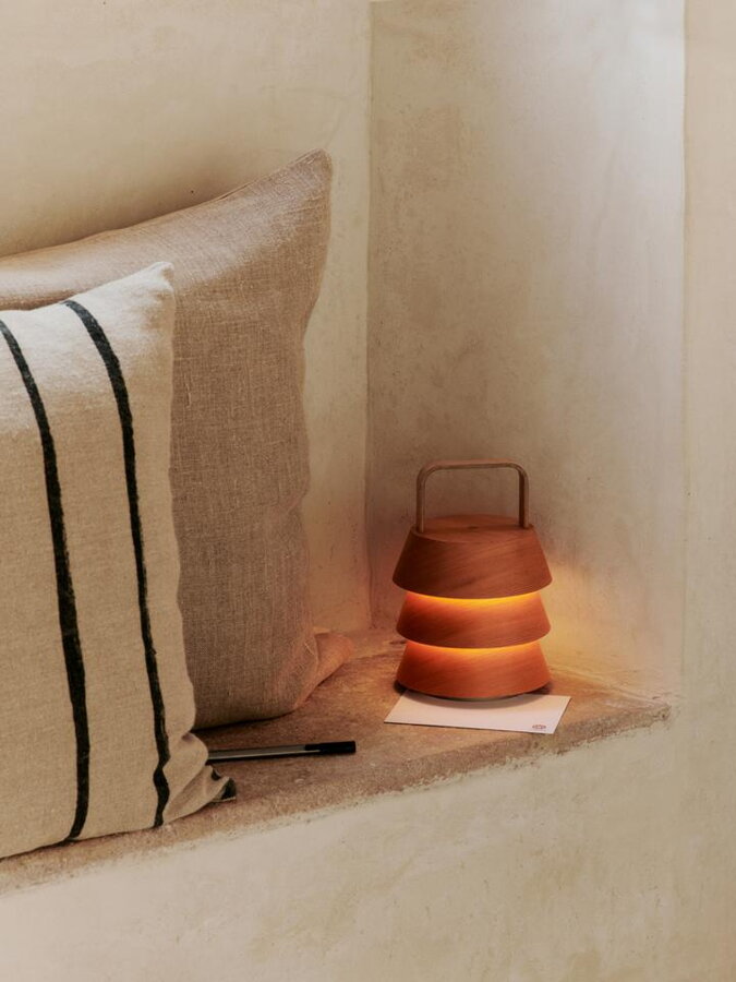 Drevená lampa položená vedľa dvoch béžových vankúšov na múriku steny.