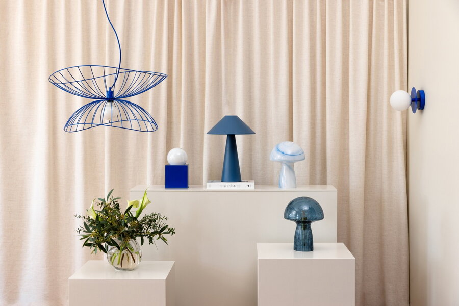 Viacero modrých a bielych stolových lámp rozmiestnených v miestnosti na bielych podstavcoch.