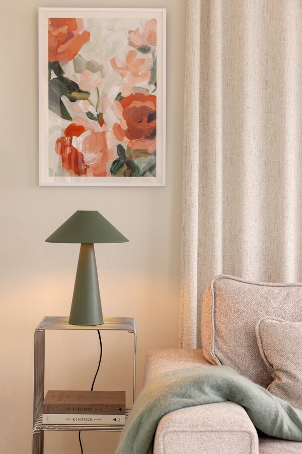 Zelená kovová stolová lampa na bielej skrinke vedľa béžovej pohovky.