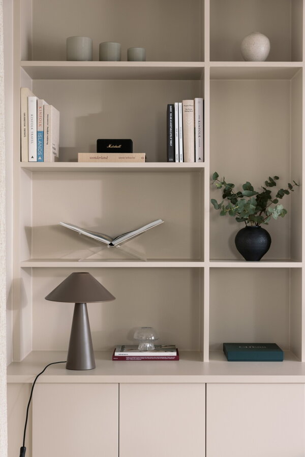 Hnedá stolová lampa v bielej policovej stene s daľšími knihami a dekoráciami.