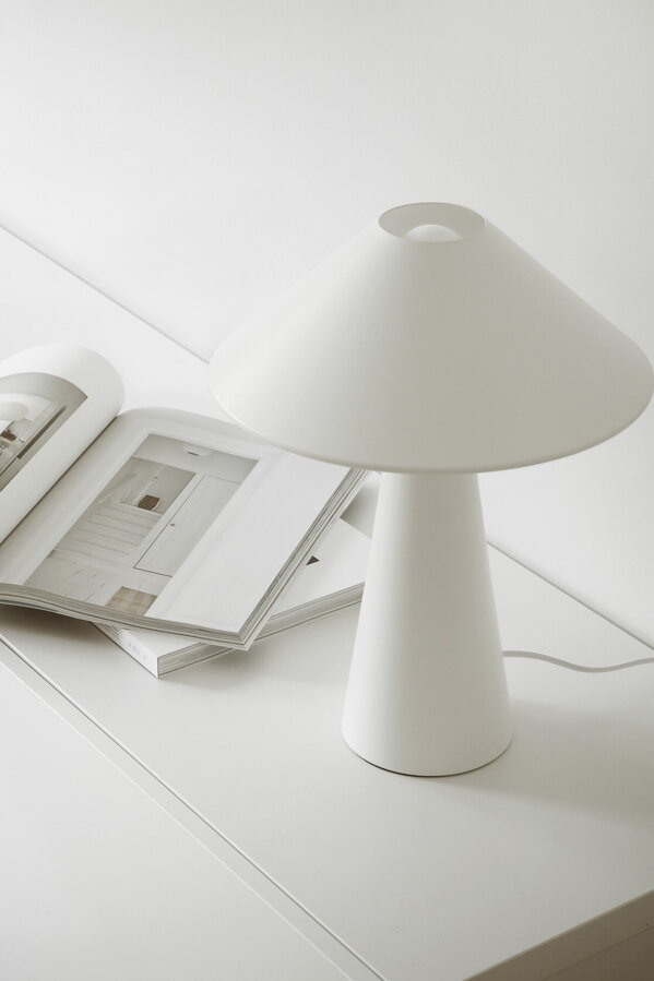 Biela kovová stolová lampa na bielej skrinke vedľa otvorenej knihy.
