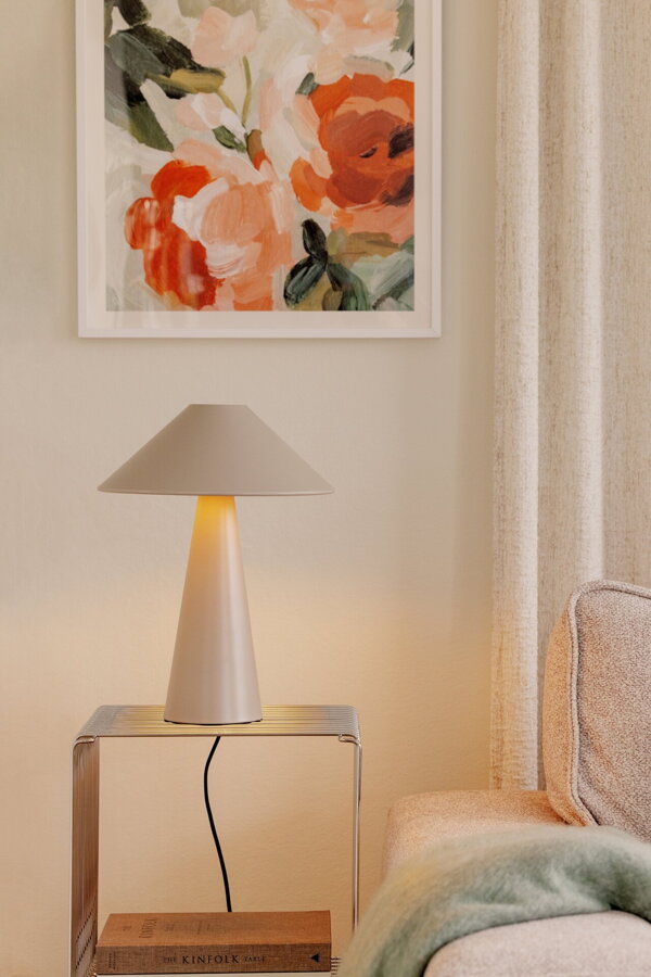 Svetlá hnedosivá stolová lampa Cannes z matného lakovaného kovu na bielom príručnom stolíku vedľa pohovky.