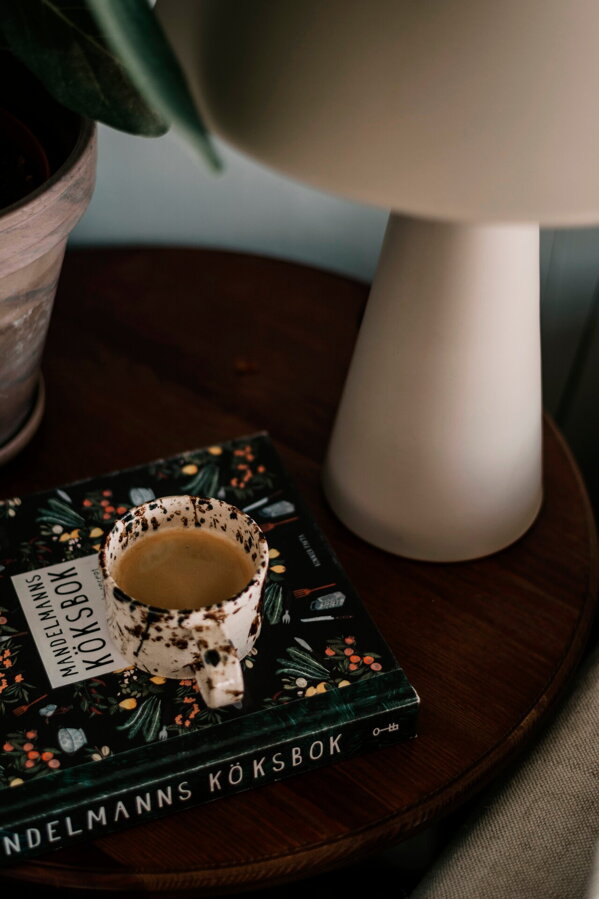 Svetlá hnedosivá stolová lampa Cannes z matného lakovaného kovu na tmavom stole vedľa šálky s kávou.