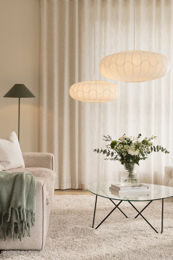 Zelená kovová stojanová lampa v rohu obývačky vedľa béžovej pohovky.