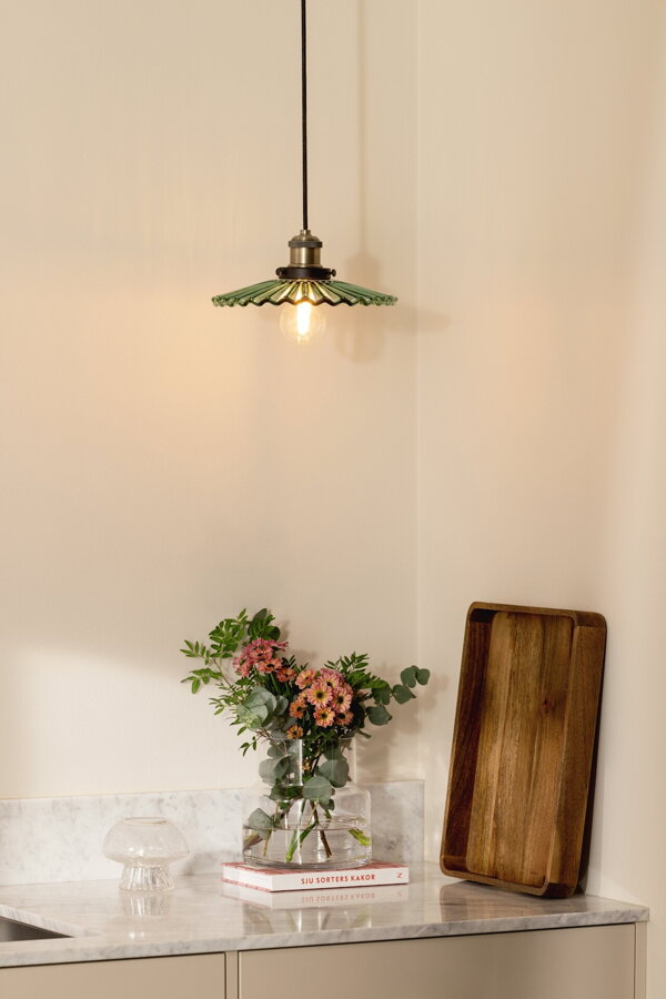 Závesná lampa s tienidlom so zeleným skleneným vlnitým tienidlom nad kuchynskou linkou.