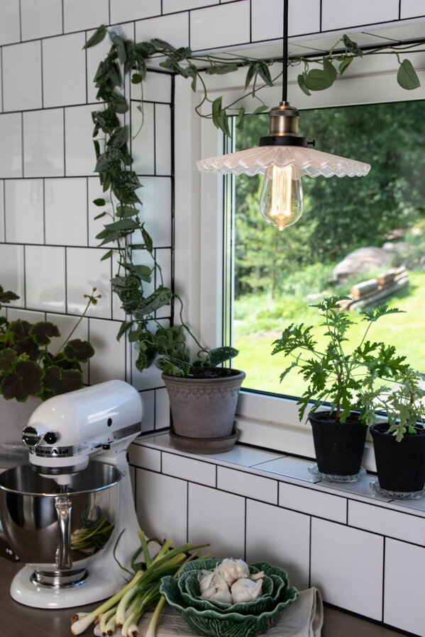Závesná lampa Cobbler s bielym skleneným tienidlom nad kuchynskou linkou pred oknom.